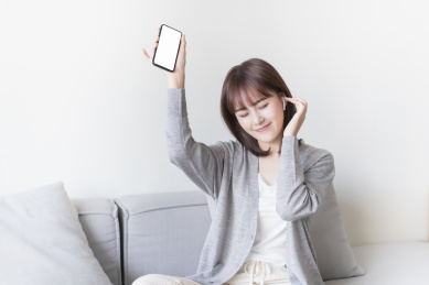 女生坐在沙发上一边用手机听音乐一边摇摆