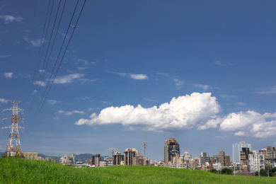 堤防公园绿草岥上的电塔，蓝天白云下的城市