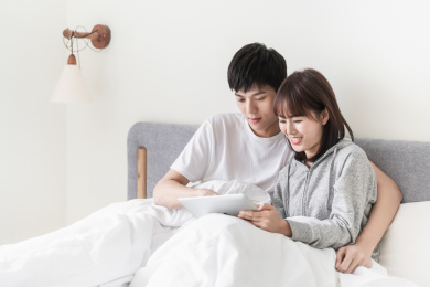 年轻夫妇坐在床上一起看平板电脑