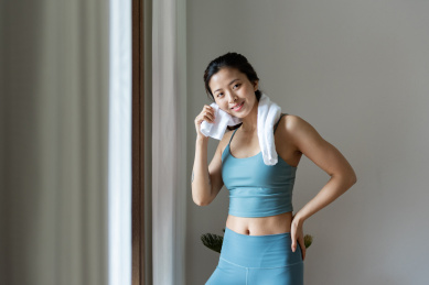 一位年轻的亚洲女性在窗边用毛巾擦汗