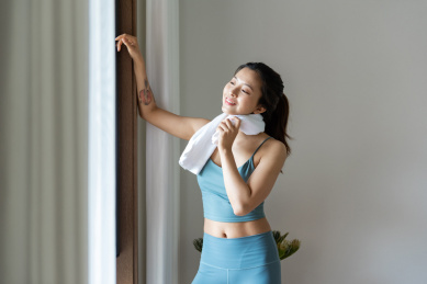 一位年轻的亚洲女性在窗边用毛巾擦汗