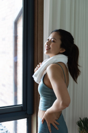 一位年轻的亚洲女性在窗边用毛巾擦汗