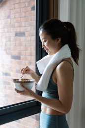 一位年轻的亚洲女性在窗边吃健康的绿色蔬菜