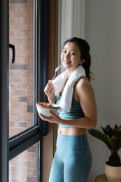 一位年轻的亚洲女性在窗边吃健康的绿色蔬菜