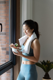 一位年轻的亚洲女性在窗边吃健康的绿色蔬菜