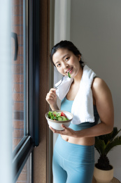 一位年轻的亚洲女性在窗边吃健康的绿色蔬菜