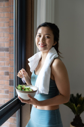 一位年轻的亚洲女性在窗边吃健康的绿色蔬菜