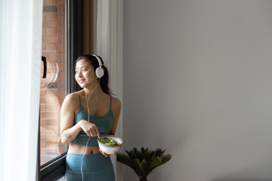 一位年轻的亚洲女性在窗边吃健康的绿色蔬菜