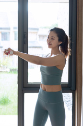一位年轻的亚洲女性在窗边使用哑铃锻炼锻炼