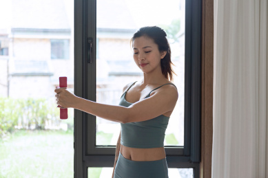 一位年轻的亚洲女性在窗边使用哑铃锻炼锻炼