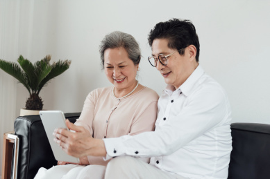 一对亚洲的老年夫妻在沙发上使用电子设备