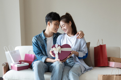 一对年轻的亚洲情侣在沙发上互送礼物