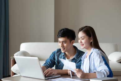 一对年轻的亚洲情侣在坐在地毯上使用电脑