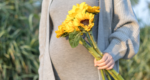 户外公园里一名孕妇的腹部特写和一束向日葵