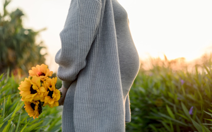 黄昏公园里一名孕妇的腹部特写和一束向日葵