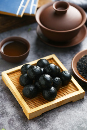 黑芝麻丸和紫砂茶具放在深色背景上