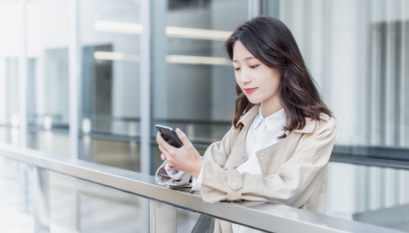 年轻亚洲商务人士靠在栏杆旁看手机