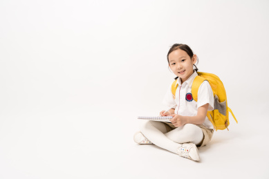 坐在白色背景前在作业本书上写的中国女孩