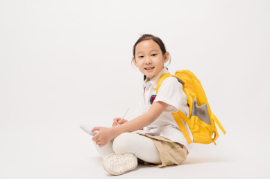 坐在白色背景前在作业本书上写的中国女孩