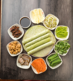 暗色木纹桌面上放着一盘卷饼和小菜