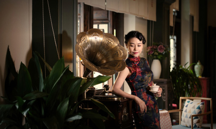 穿着旗袍的女人站在留声机旁边听音乐