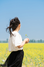 夏天站在油菜花田边拿着野花的女孩