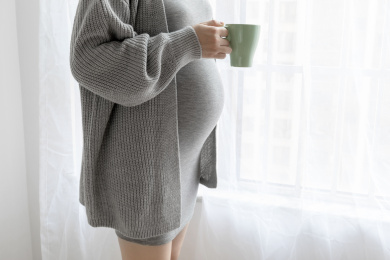 窗边一名孕妇拿着一个水杯