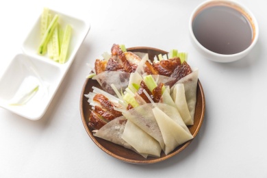 白色桌面上放着一盘卷好鸭肉的春饼