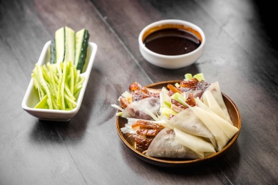 暗色木纹桌上放着一盘卷好肉的春饼