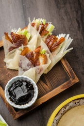 暗色木纹桌上放着一盘卷好肉的春饼