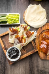 暗色木纹桌上放着一份烤鸭与卷好肉的春饼