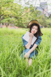 长发少女抱着书闭眼坐在草丛中