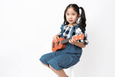 坐在白色背景前弹奏尤克里里的女孩