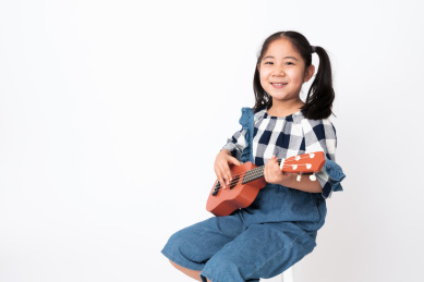 坐在白色背景前弹奏尤克里里的女孩