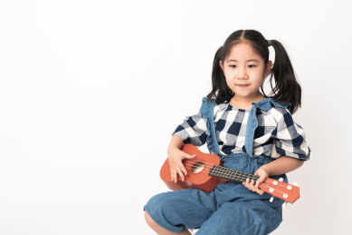 坐在白色背景前弹奏尤克里里的女孩