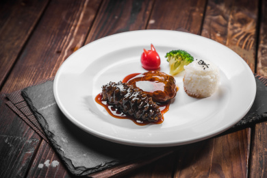 棕色木纹桌面上放着一盘鲍汁花菇辽参扣饭