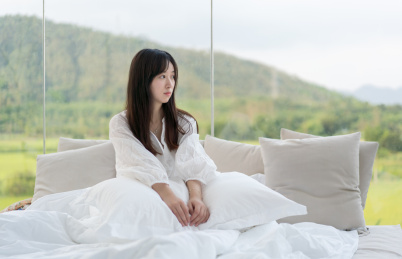 年轻长发女性半坐在床上看旁边发呆