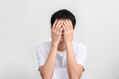 白色背景前捂住脸的年轻人