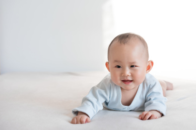 穿粉蓝和尚衣的九个月婴儿趴卧着笑