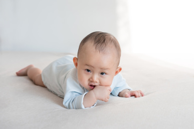 正在趴着咬手的九个月婴儿