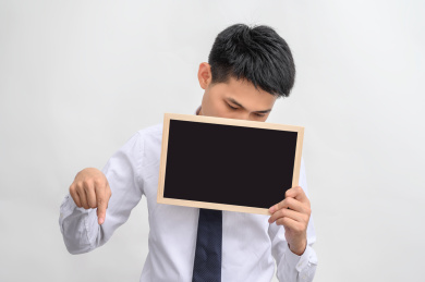 白色背景前拿着黑板手指向下指的商务男性