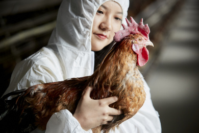 身穿防护服怀抱家禽的年轻女性饲养员