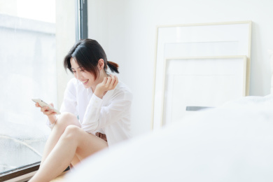 在窗边使用手机的年轻亚洲女性