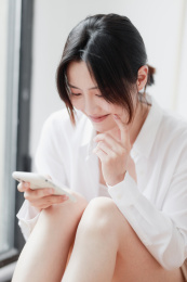 在窗边使用手机的年轻亚洲女性