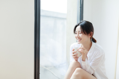 靠在窗边喝咖啡的年轻亚洲女性