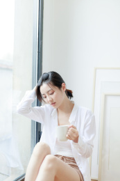 靠在窗边喝咖啡的年轻亚洲女性