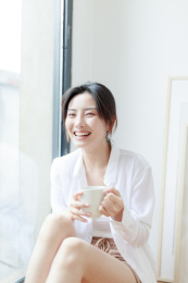 靠在窗边喝咖啡的年轻亚洲女性