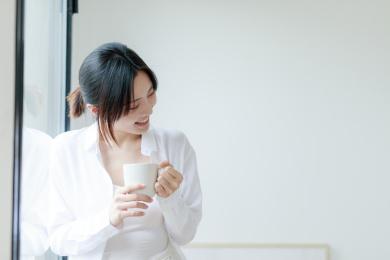 靠在窗边喝咖啡的年轻亚洲女性