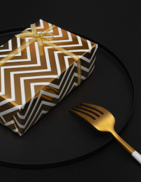 黑色背景盘子里的黑金礼物盒与叉子