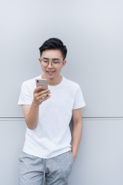 亚洲青年站在墙边笑着玩手机
